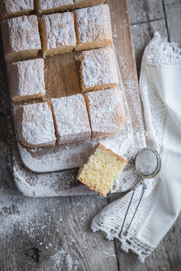 Blick von oben auf ein Holzbrett mit Pasiego-Kuchen, einem typischen Kuchen aus Katalonien in Spanien, bestreut mit Zucker auf einem rustikalen Holztisch