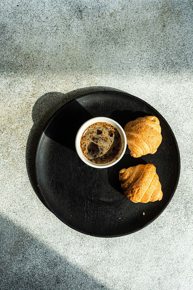Draufsicht auf einen schwarzen Kaffee und frisch gebackene Croissants auf einem Betontisch