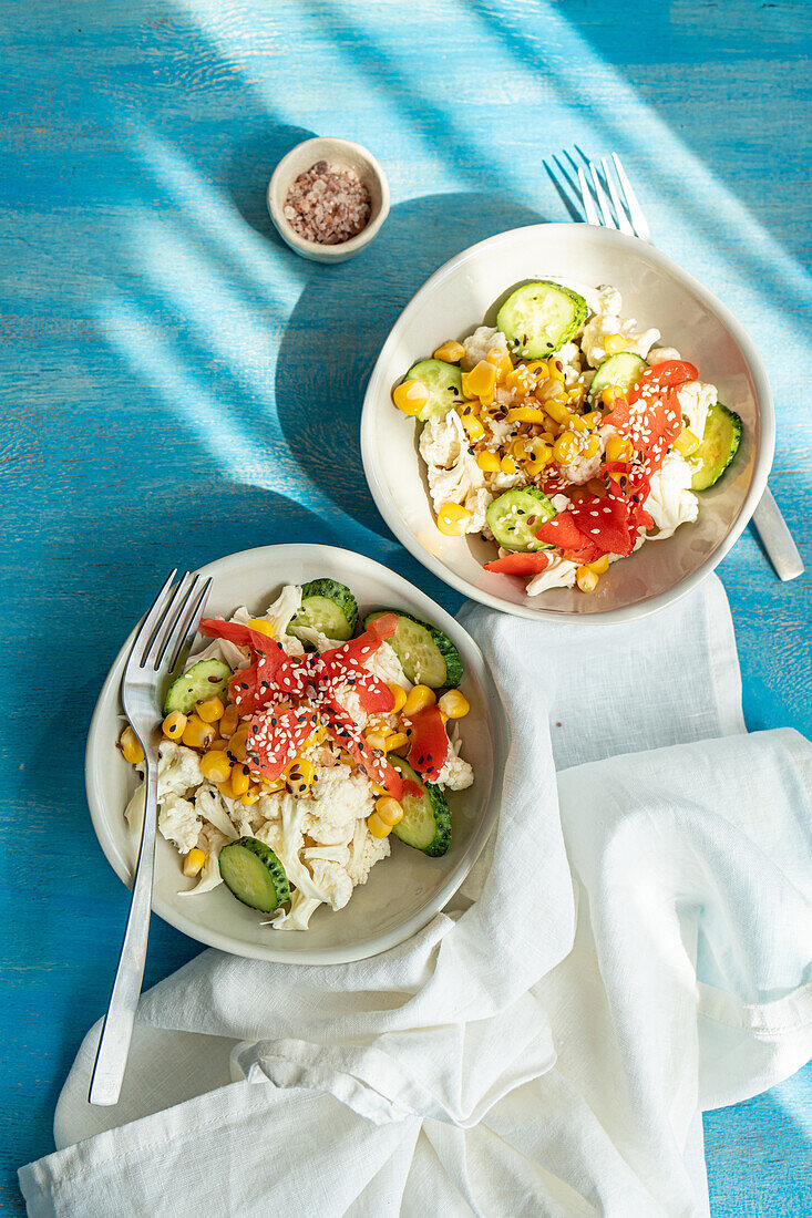 Gesunde Salate mit verschiedenen Gemüsesorten, serviert in einer Schüssel mit Gabel auf einem Tisch mit blauem Hintergrund (Draufsicht)