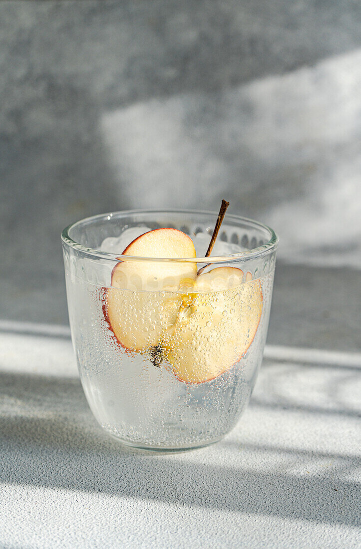 A close-up view of a glass of tonic water with a slice of apple, highlighting the drink's bubbles and refreshing appearance