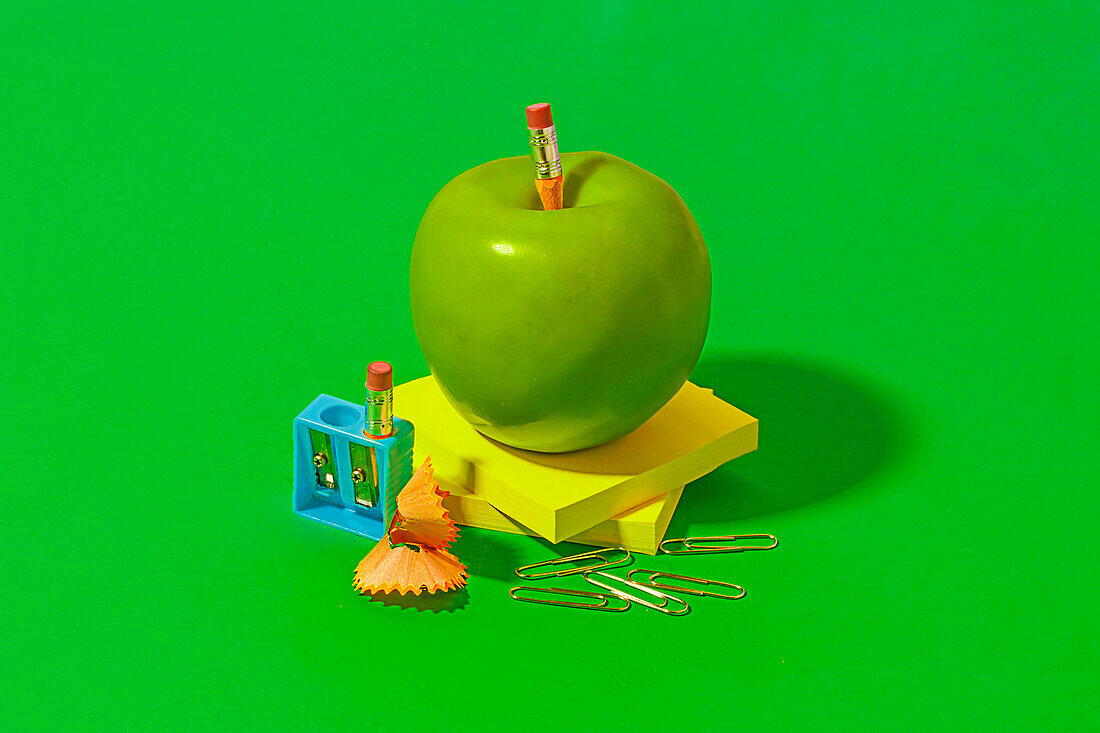 Granny Smith apple placed on sticky notes near office or school supplies on bright green background