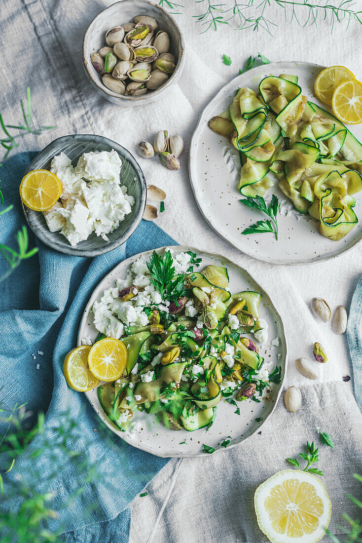 Draufsicht auf einen leckeren gesunden gegrillten Zucchinisalat mit Fetakäse und Pistazien, serviert mit Zitronenscheiben und Kräutern auf dem Tisch
