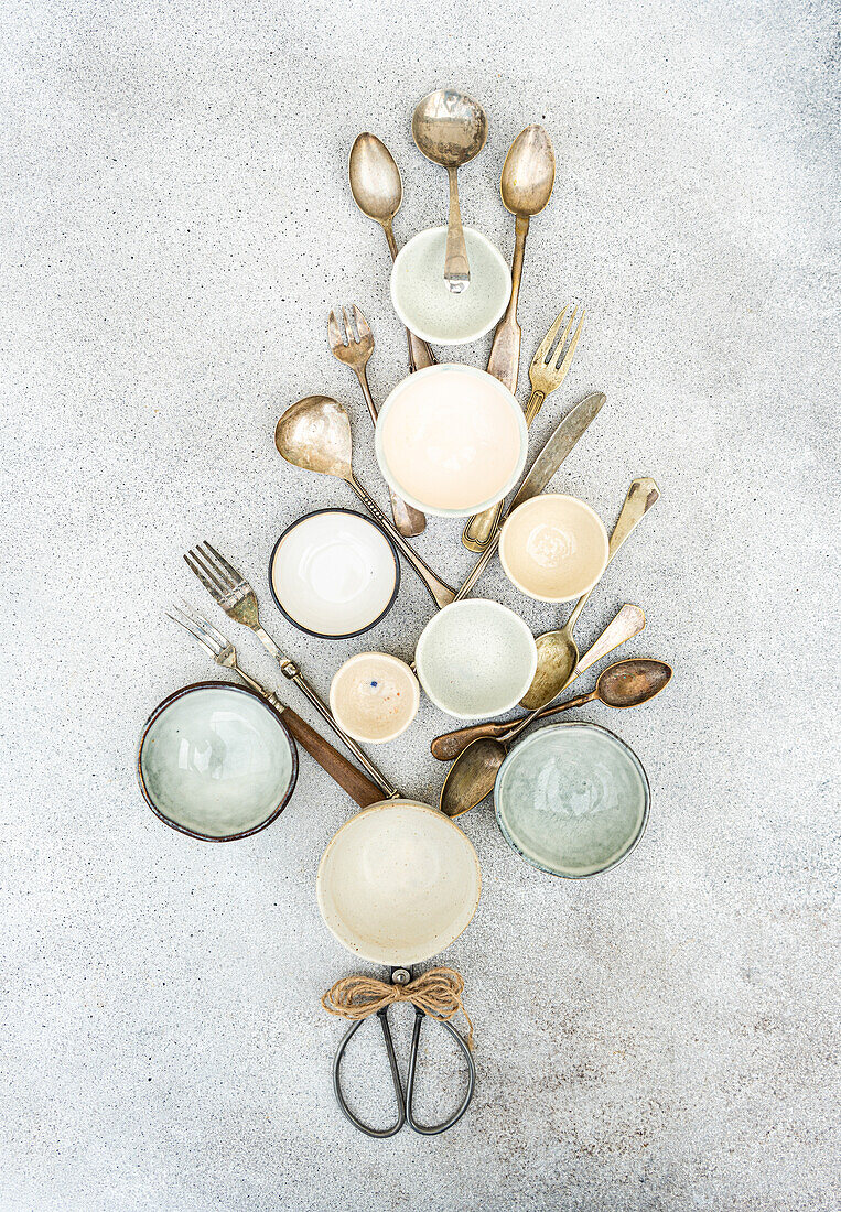 Overhead view of rustic kitchen utensils and empty bowls arranged symmetrically on a textured background in a christmas tree shape.