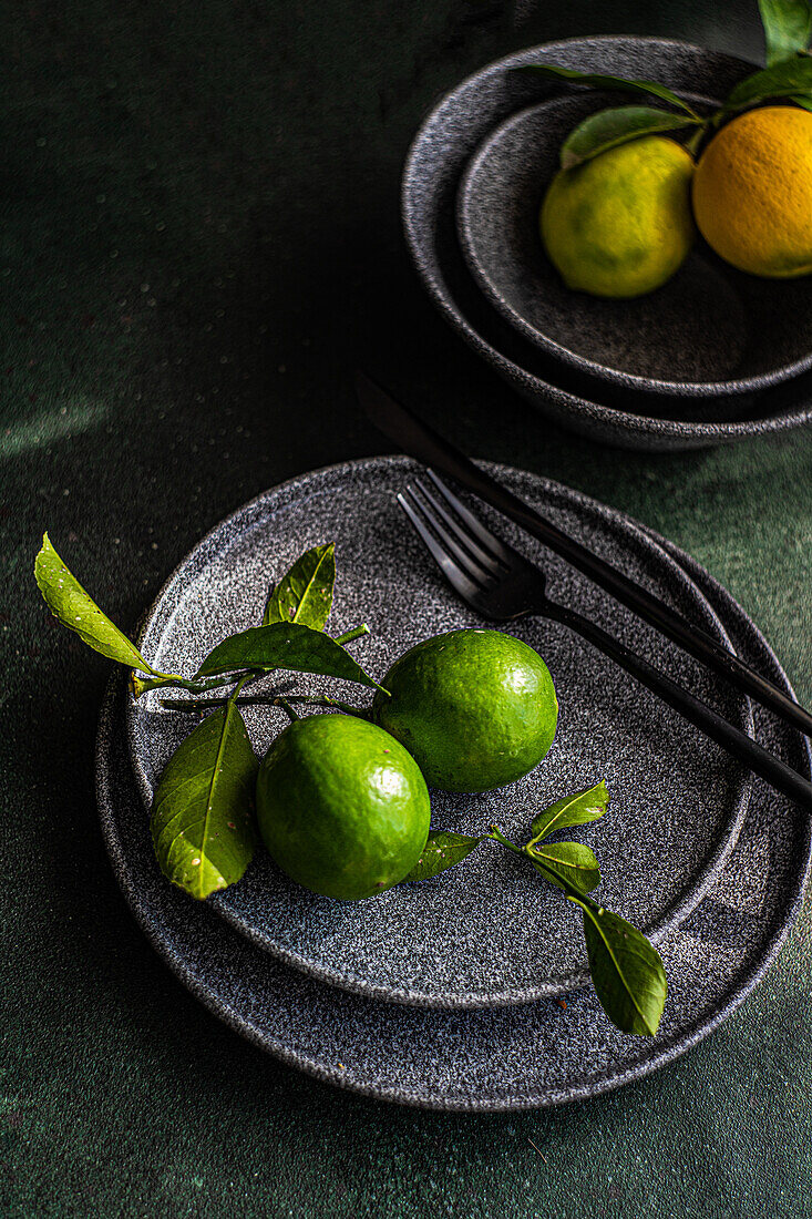 Fresh green limes on a dark ceramic plate with a fork, against a dark background with soft lighting.