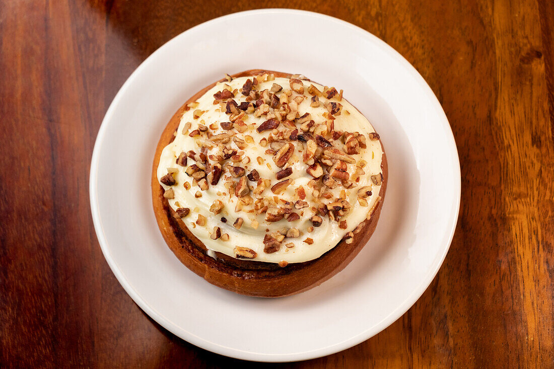 Top view of appetizing homemade cake with sweet cream and nuts on white ceramic plate over wooden dining table indoors
