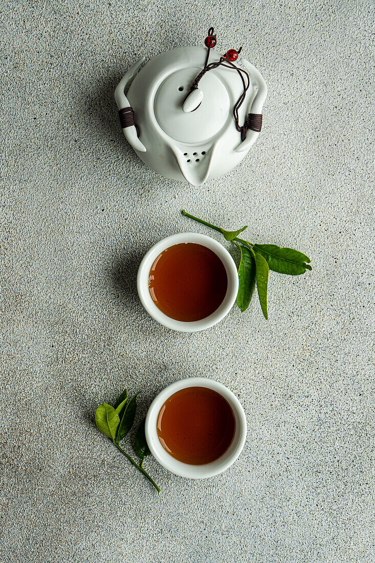 Draufsicht auf ein Teeservice im asiatischen Stil mit Zitronenblättern auf einer grauen Fläche