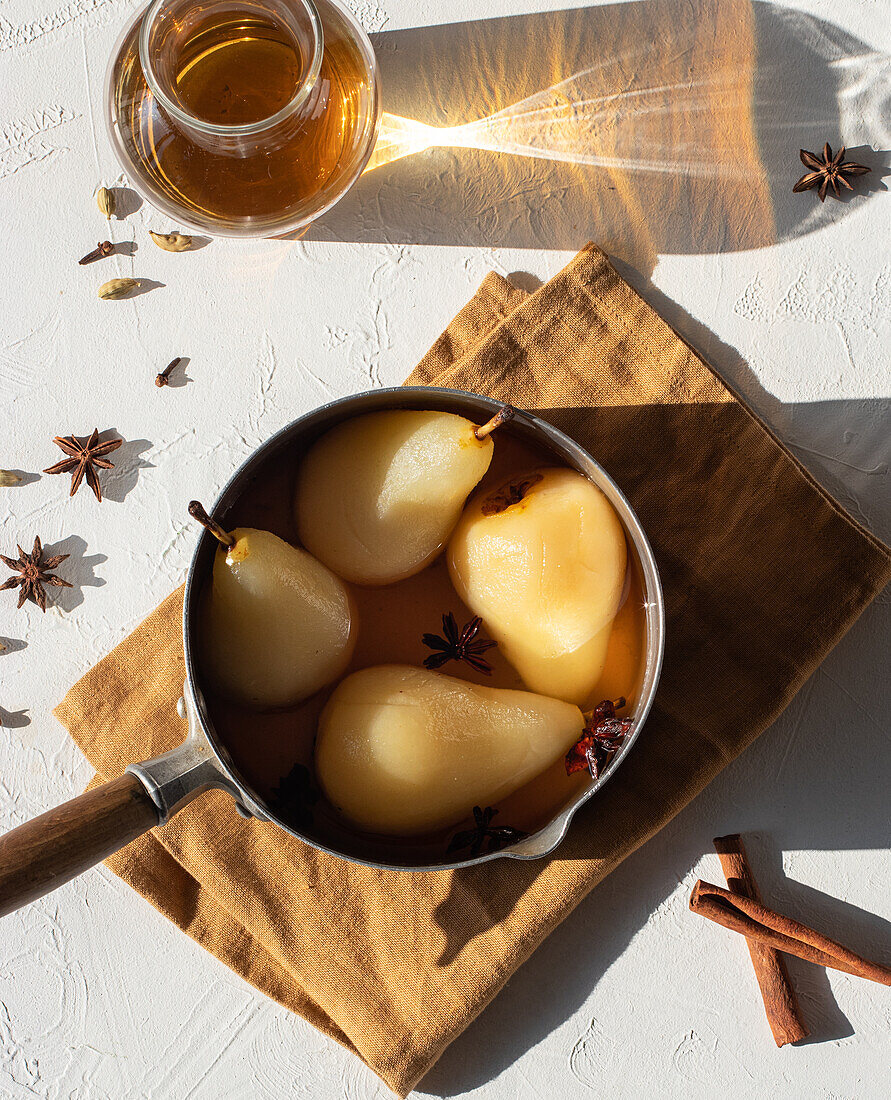 From above saucepan with delicious poached pears in white wine at table near star anise and jar with juice