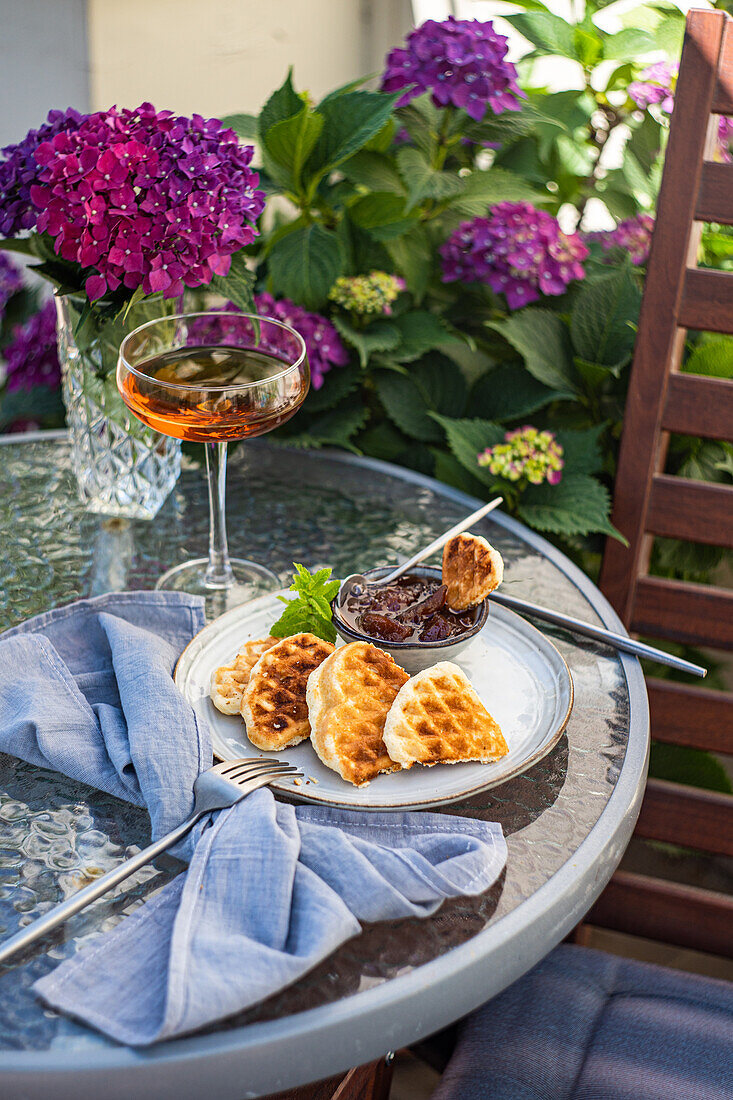 High angle of appetizing sweet waffles served with peach jam on round table near glass with drink in garden with blooming purple Hydrangea flowers