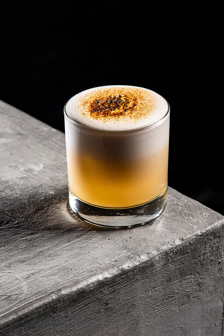 High angle of delicious whiskey sour cocktail with foam served in glass placed against black background
