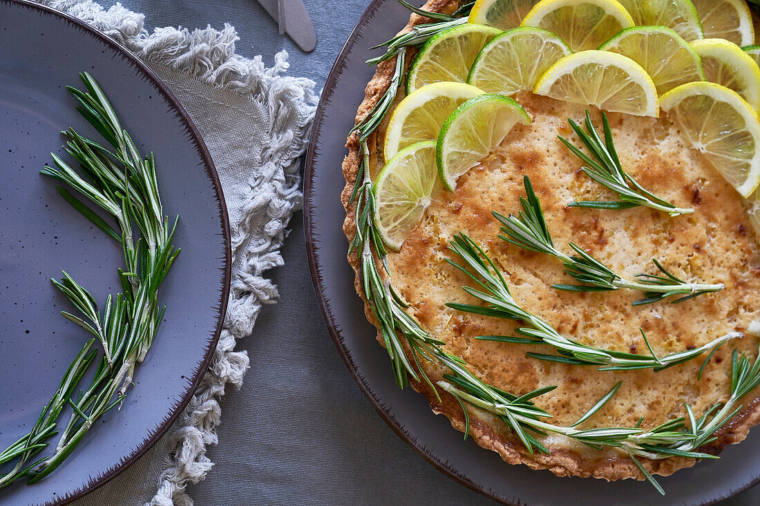 From above of round lemon pie with decorated with lemon slices and rosemary sprigs on table in the kitchen