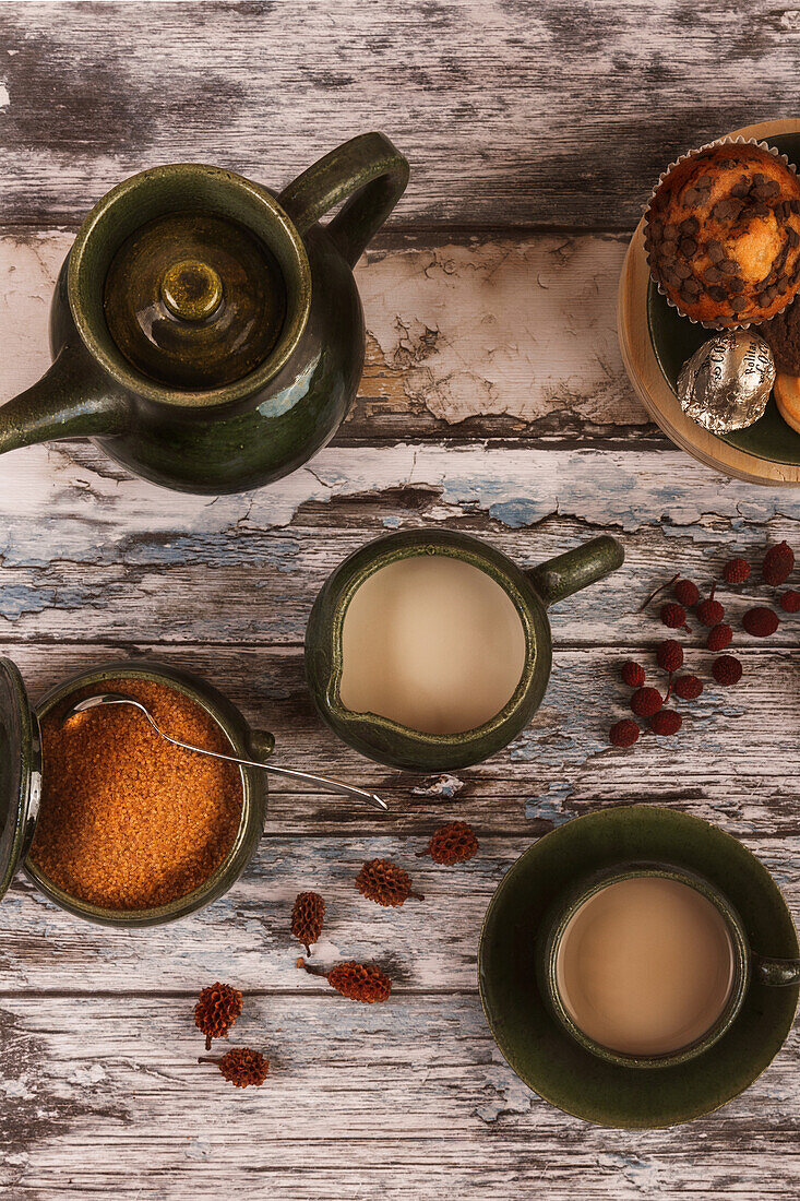A top-down view of a cozy tea arrangement featuring two cups of tea, a green teapot, spices, and dried fruits on a rustic wooden table.