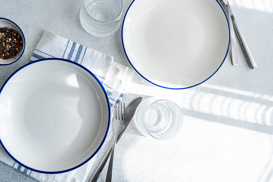 Draufsicht auf einen gedeckten Tisch mit weißen Tellern mit blauen Rändern, Silberbesteck und Gläsern auf einer Leinentischdecke