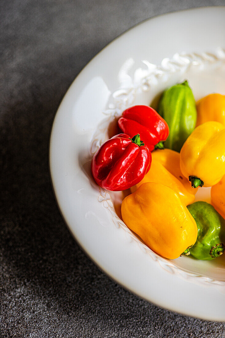 Top view of different colored peppers placed in a round white ceramic plate on a concrete background