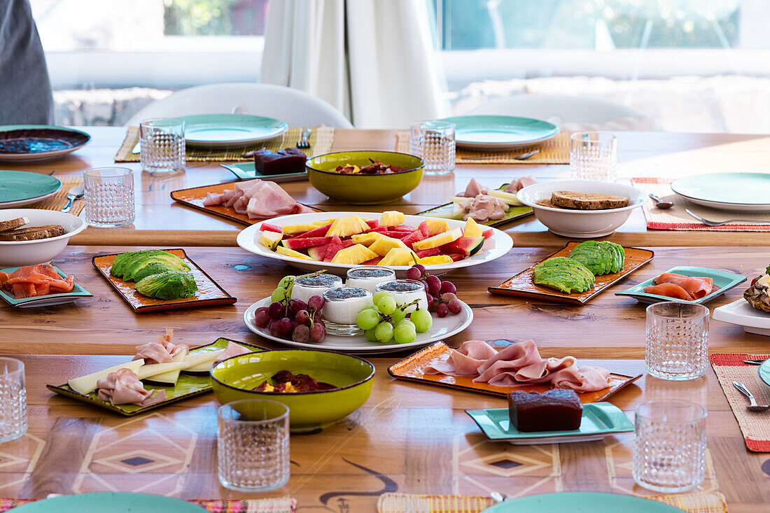 High angle of delicious sliced fruits, ham, avocado and dessert served on plates placed on table for breakfast in morning