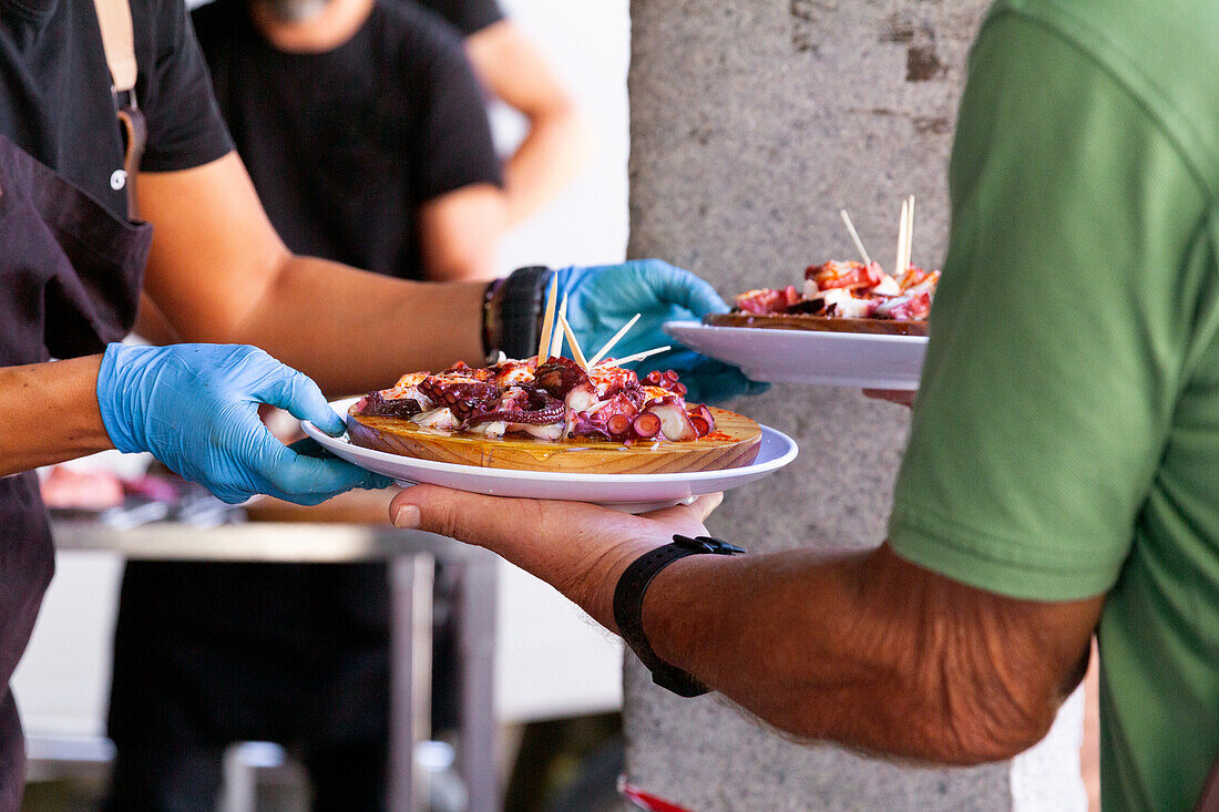 Anonymer Koch mit Handschuhen, der einem Kunden einen Teller mit frisch zubereiteten Oktopus-Tapas überreicht