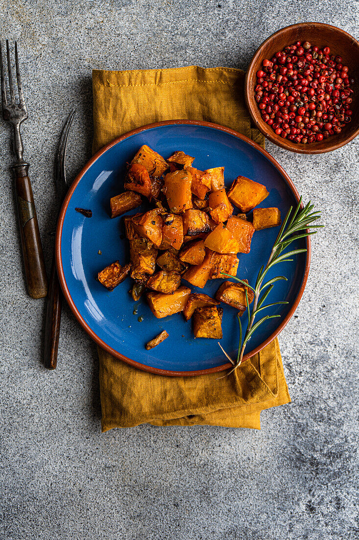 Baked spicy pumpkin cubes served on blue ceramic plate on the table