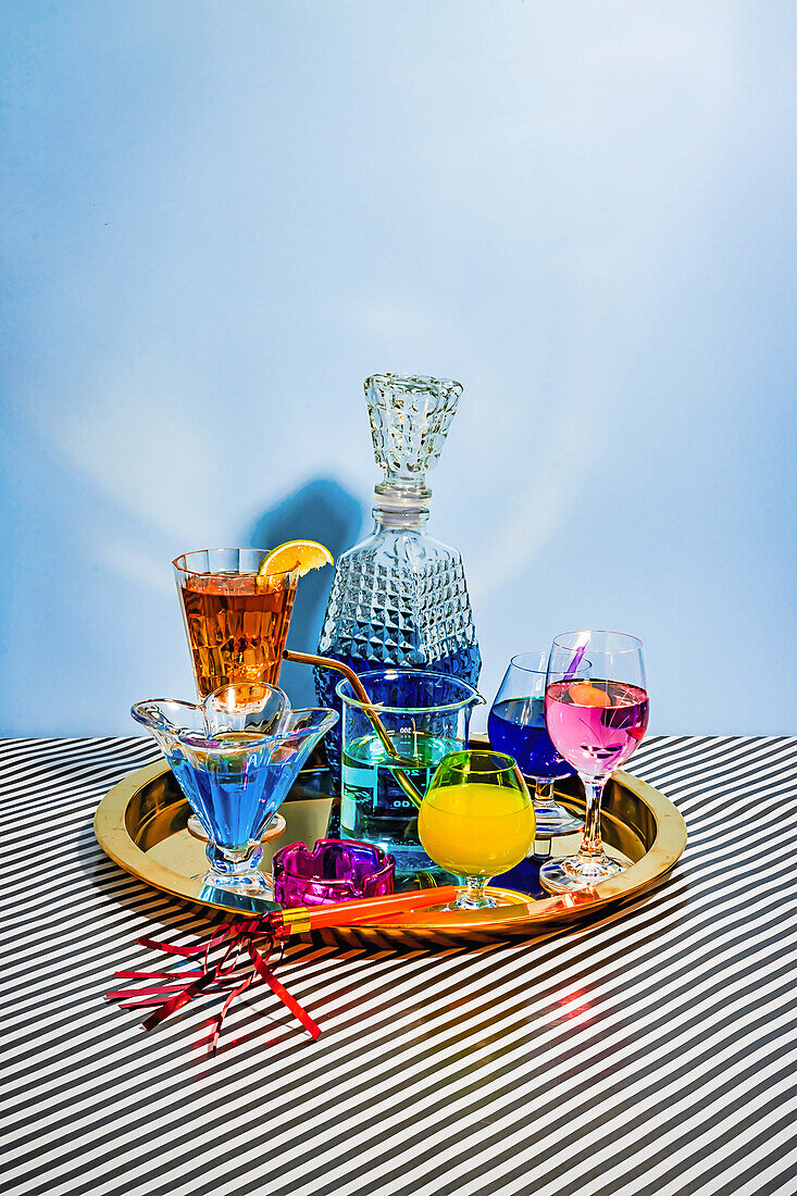 From above different varieties of cocktails comprising blue margarita Long Iceland iced tea wine daiquiri in attractive glasses and jar placed on plate on striped cloth against blue background