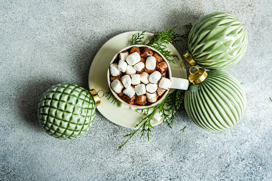 Draufsicht auf leckeren Kakao mit Marshmallow auf einem Teller mit Tannenzweigen in der Nähe von Weihnachtskugeln