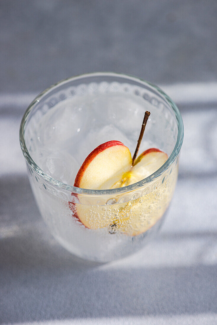 Nahaufnahme eines Glases Tonic Water mit einer Apfelscheibe von oben, wobei die Bläschen und das erfrischende Aussehen des Getränks hervorgehoben werden