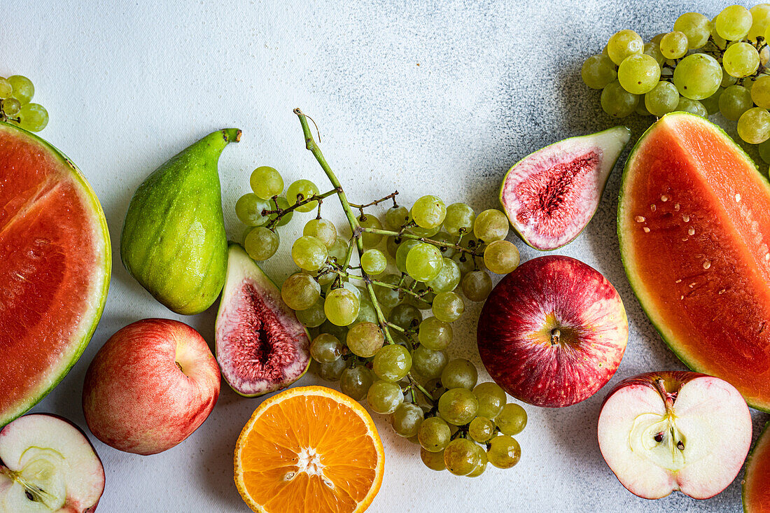 Draufsicht auf einen Rahmen mit Früchten der Saison, bestehend aus Wassermelone, Orange, Birne, Weintrauben und Äpfeln, auf einer weißen Fläche