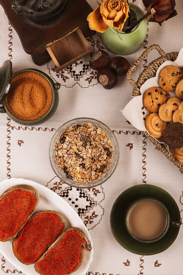Gemütliches Frühstück mit Gebäck, Müsli, Kaffee und Tomatentoasts auf einer gemusterten Tischdecke