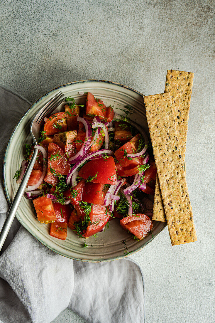 Von oben Schale mit Salat aus Tomaten, roten Zwiebeln und Dillkraut auf einem Marmortisch