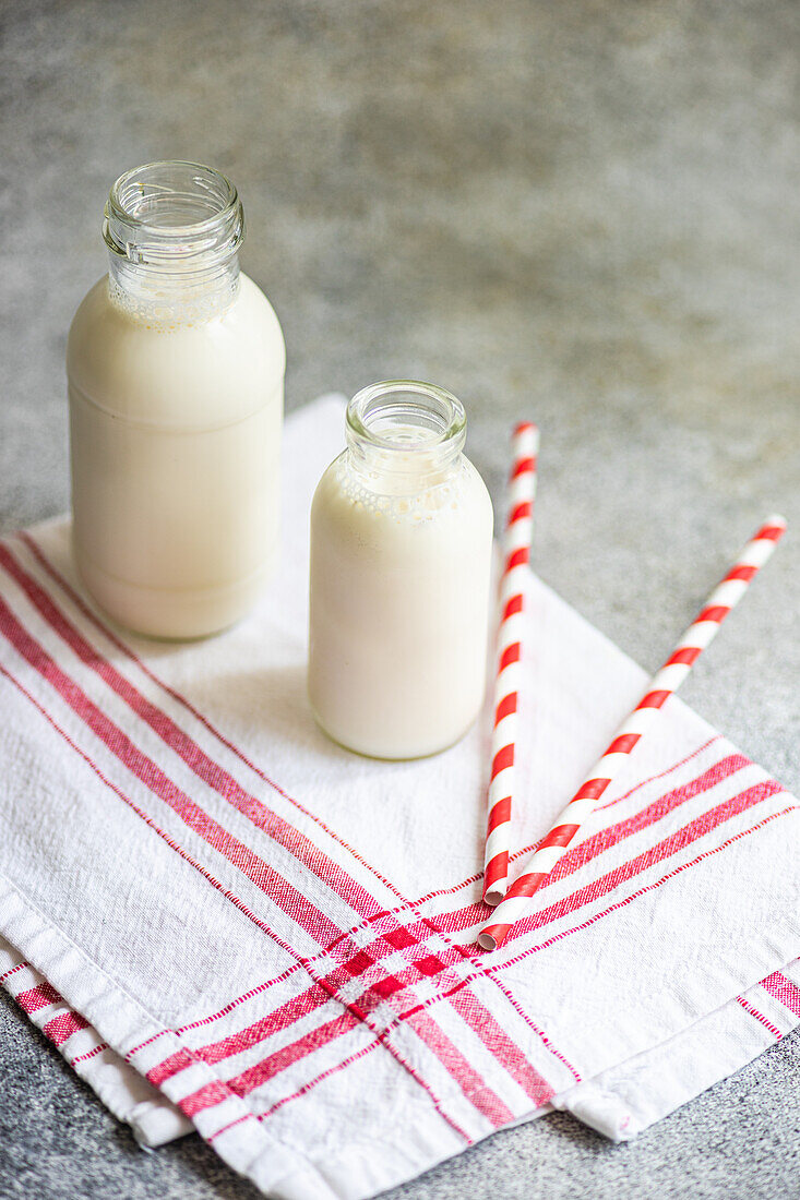 High angle of raw cow milk in vintage bottles on rustic napkin and drinking straws against gray surface