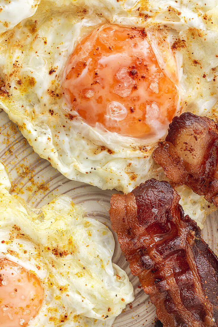 Tasty sunny side up eggs with fried bacon strips on plate