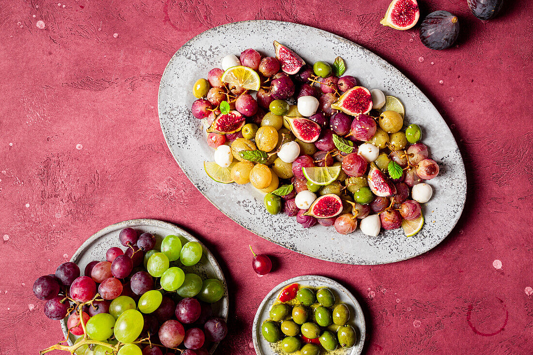 Frische reife Trauben, Oliven, Feigen und Mozzarella auf einem Teller auf rotem Tischhintergrund