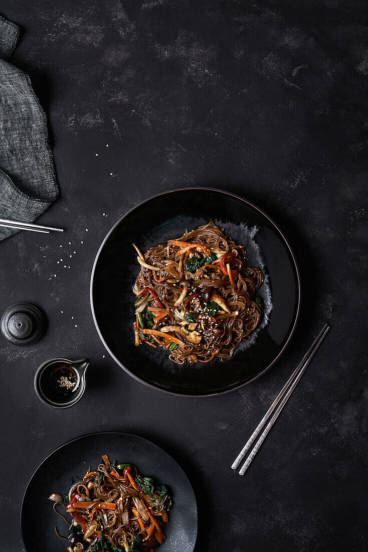 Top view chopsticks and plate with Korean dish Japchae cooked from noodles and vegetables