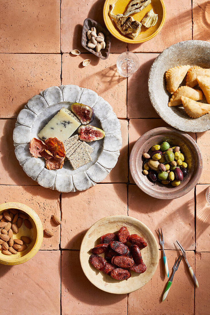 Draufsicht auf spanische Mezze mit verschiedenen Käsesorten und Nüssen neben Oliven und Chorizzo auf dem Tisch