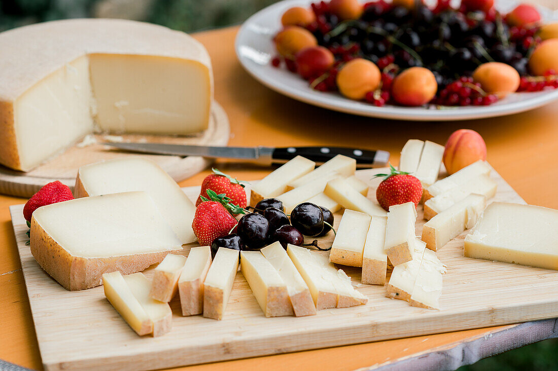Slices of delicious Parmesan cheese and fresh strawberries cherries and apricots served on wooden cutting board on table during outdoor event