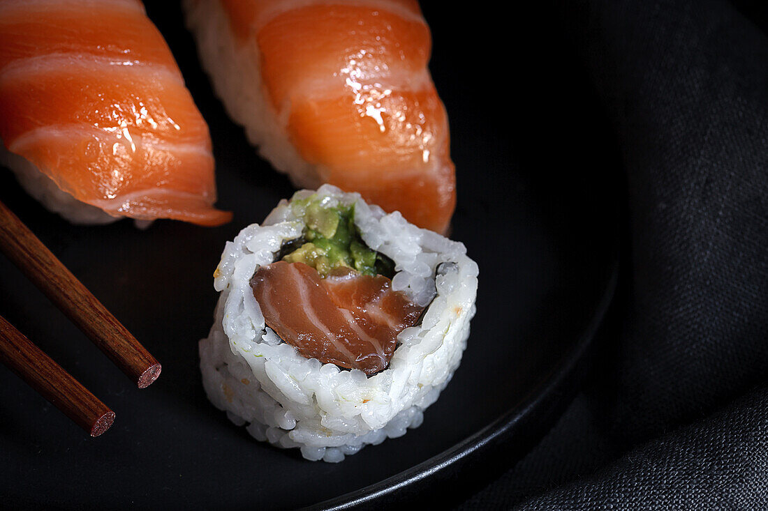 Top view composition of delicious fresh sushi and bamboo chopsticks served on black platter on checkered cloth