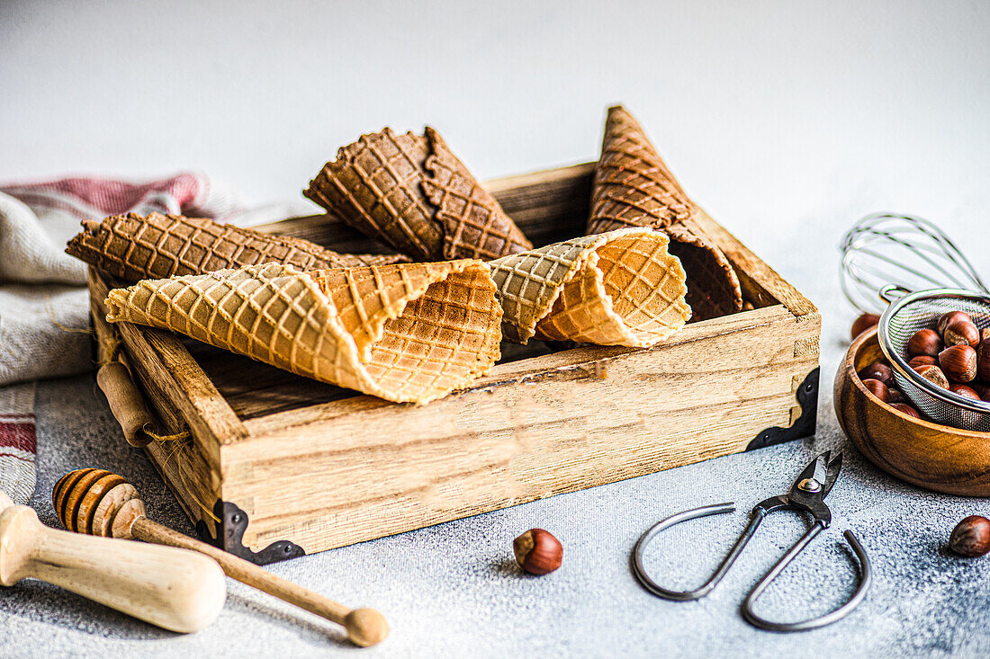 Wooden box with empty waffle cones, bowl with hazelnuts and tools for ice cream cooking