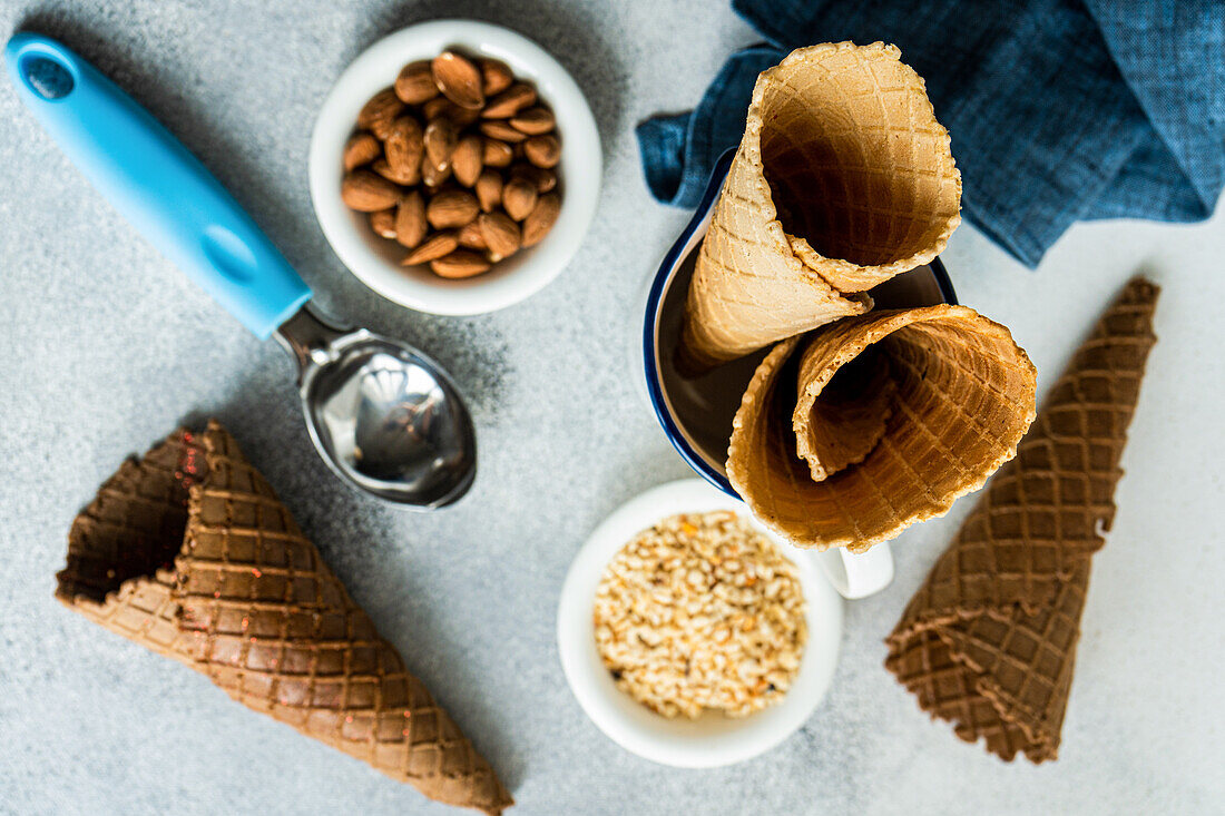 From above waffle cones and nuts for ice cream preparation on concrete table with white concrete background with towel