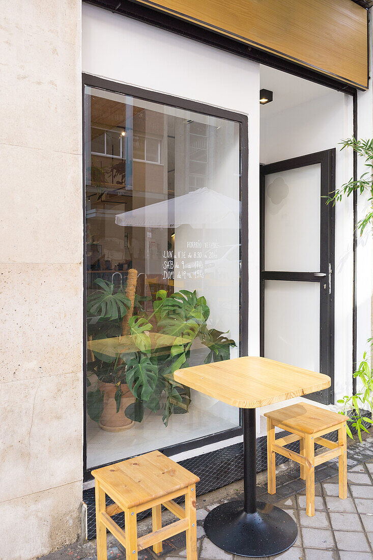 Holzstühle und Tisch auf einer gepflasterten Terrasse an der Straße in der Nähe des großen Fensters einer modernen Cafeteria mit einer grünen Topfpflanze