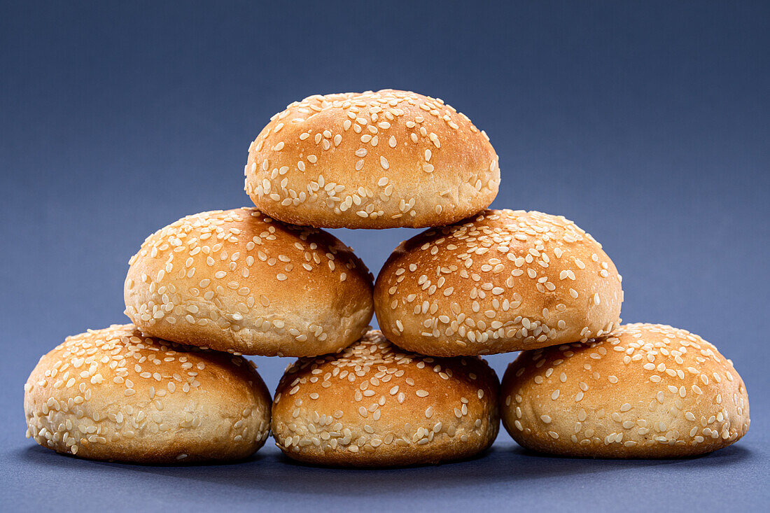 Bunch of yummy whole burger buns with sesame stacked together on blue background