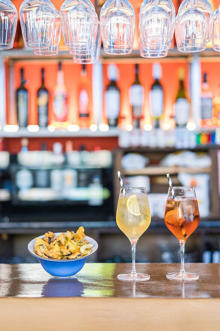 Bowl with tasty seafood appetizers and glasses of cold fresh cocktails served on wooden counter in bar