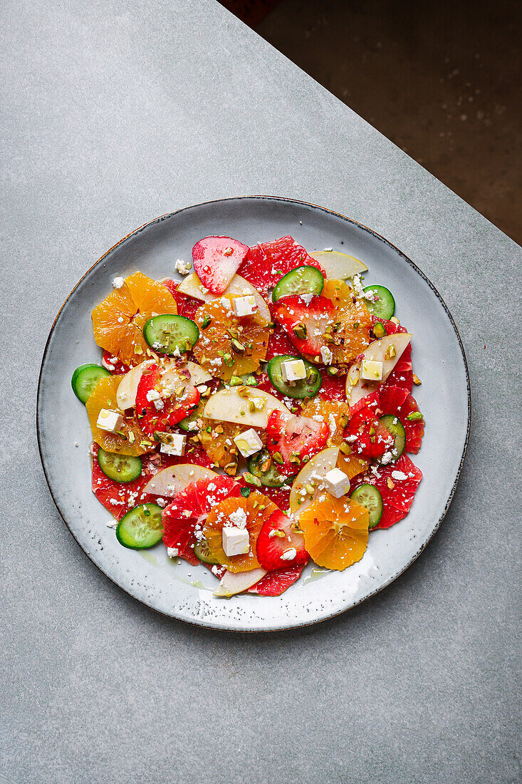 Top view of healthy salad with oranges and strawberries and apples and cucumbers served with cheese and pistachios on plate