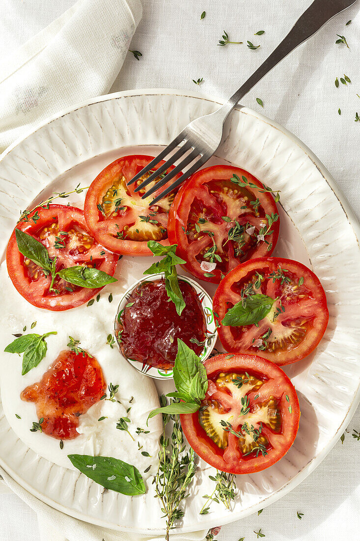 Draufsicht auf frische Tomaten- und Mozzarellascheiben mit Soße und Kräutern, serviert auf einem Teller auf einem Tisch bei Tageslicht