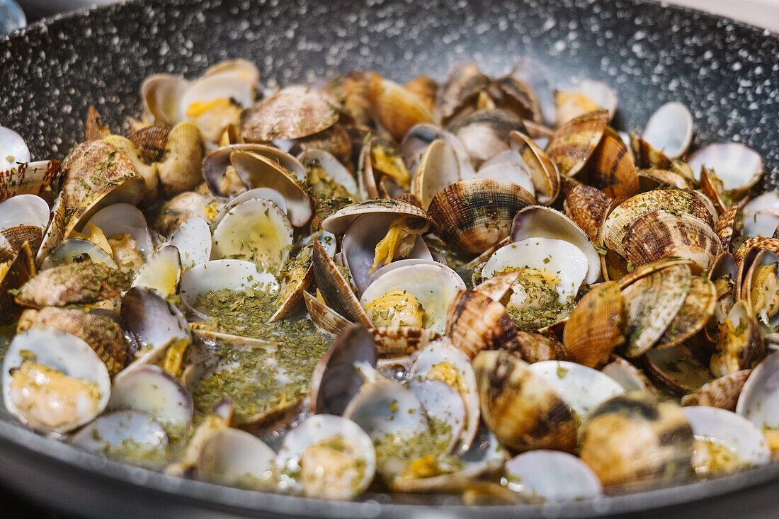 Heap of tasty mollusks with shells frying in hot black frying pan on electric cooker in light kitchen at home