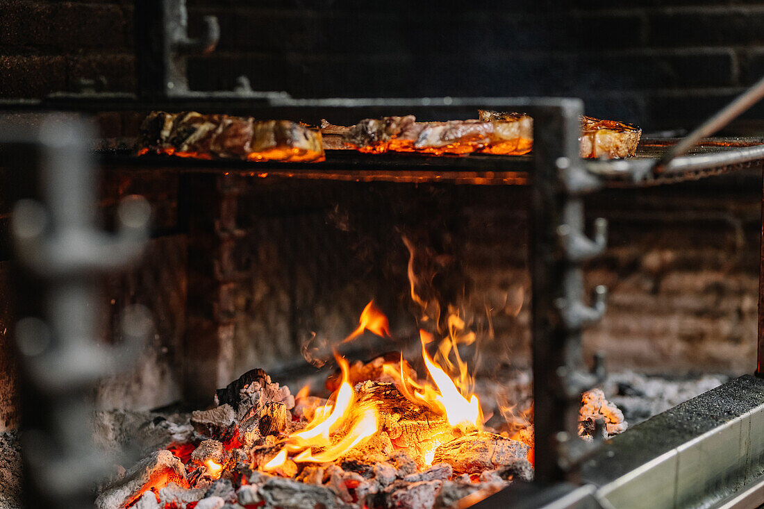 Appetizing juicy steaks placed on barbecue grid over burning flame while frying in grill oven