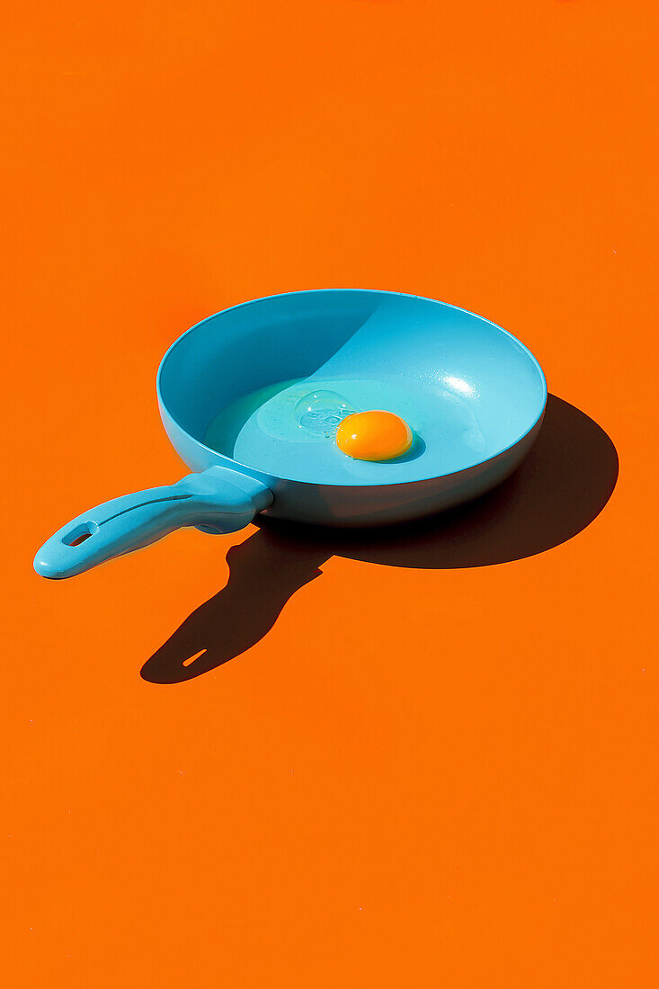 Whole raw egg yolk placed in blue frying pan with handle isolated against orange background