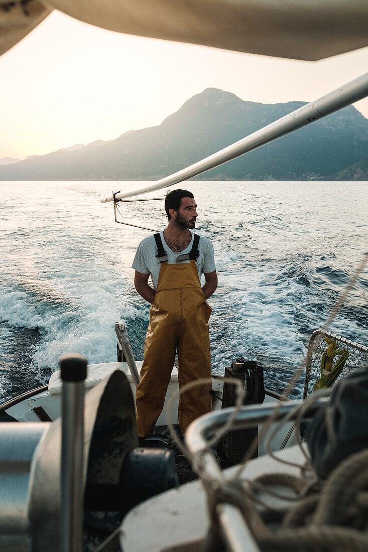 Gesamtansicht eines nachdenklichen männlichen Fischers in Uniform, der die Meereslandschaft beim Fischen in Soller nahe der Baleareninsel Mallorca bewundert