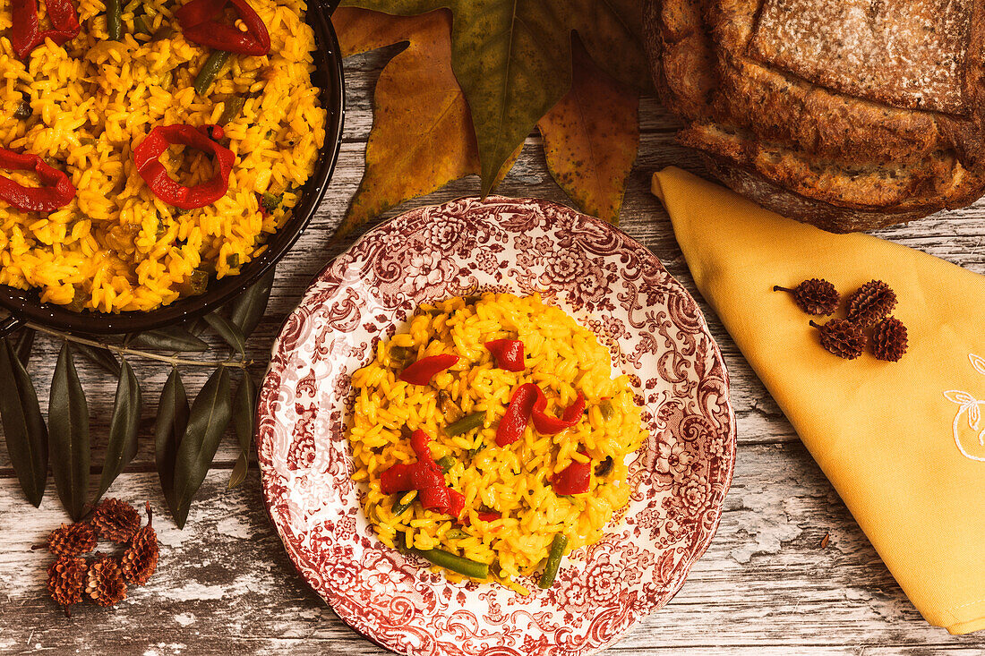Colorful rice dish garnished with veggies, accompanied by a wedge of cheese and slices of rustic bread, presented on a wooden table.