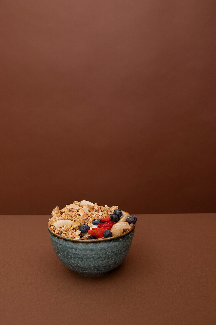 Bowl with delicious muesli and fresh sliced banana with strawberry and fruits placed on brown background in studio