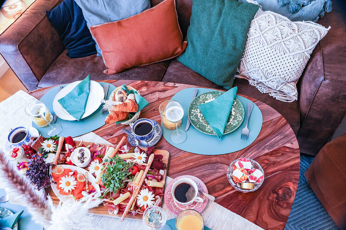 Ein hübsch gedeckter Frühstückstisch mit einer Vielzahl von Speisen auf einer rustikalen Holzfläche, umgeben von bequemen Kissen und einer gemütlichen Atmosphäre