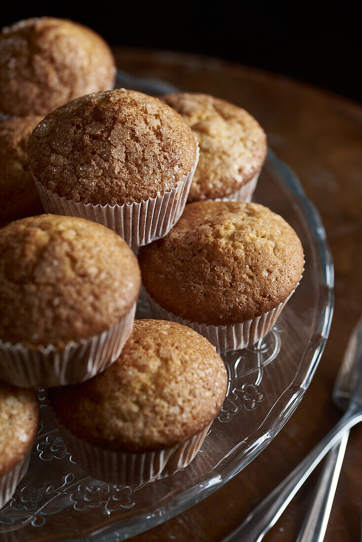 Close-up of golden-brown muffins arranged on a decorative glass serving plate, with a dark background.