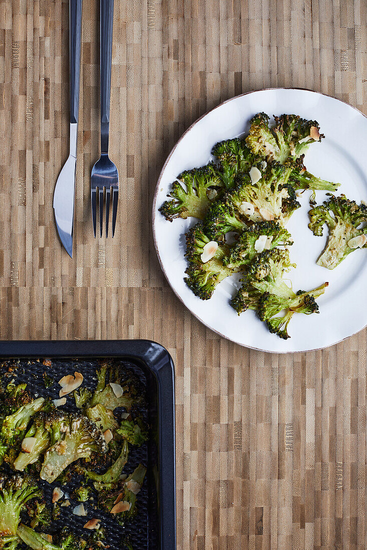 From above baked cooked green broccoli stems with cheese and pepper placed on wooden background near cutlery