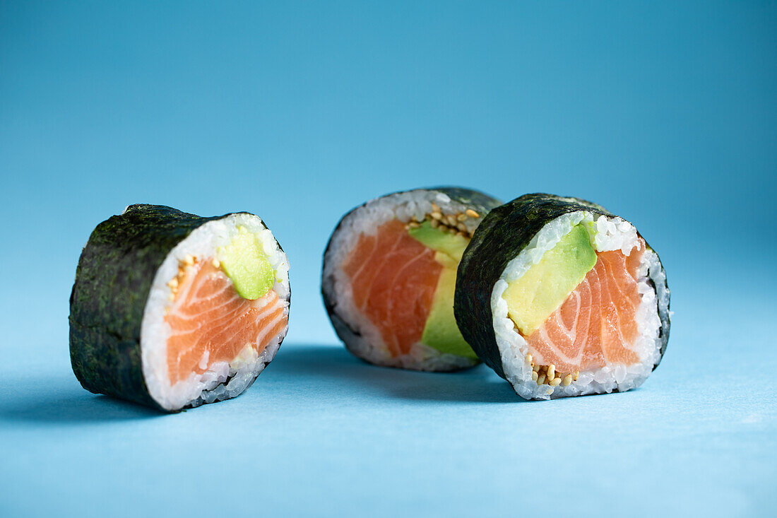 Leckere japanische Futomaki Norwegische Sushi-Rolle mit frischem Lachs und Avocado, serviert vor blauem Hintergrund in einem hellen Studio